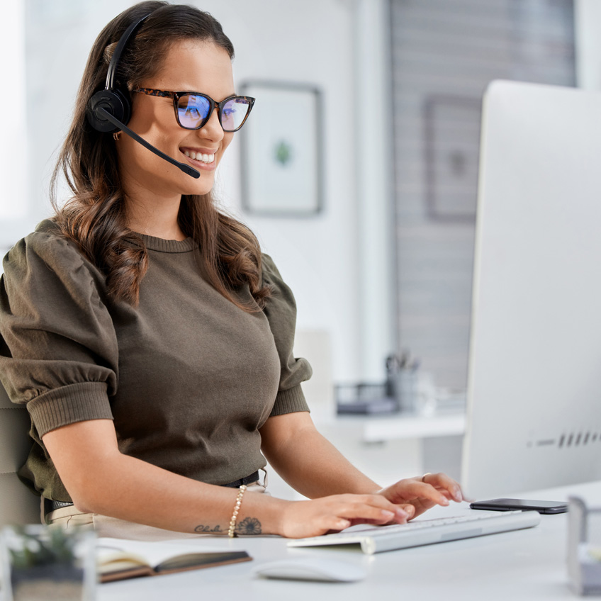 Junge Frau telefoniert, während sie am PC sitzt und tippt, sie freut sich über die neue Data Cleaning Strategie.