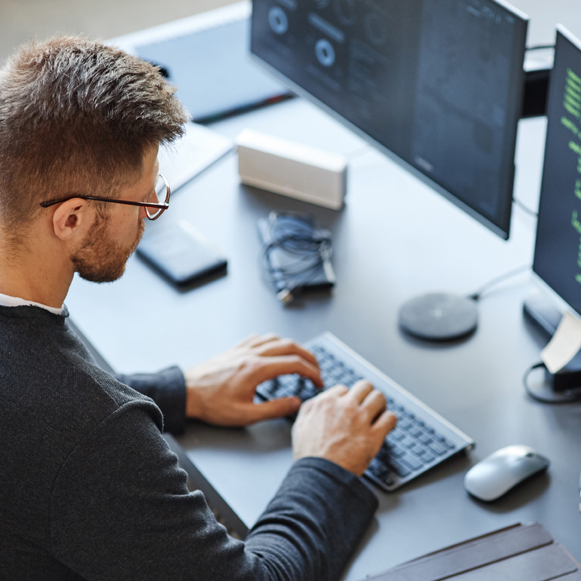 Mann arbeitet am PC mit zwei Bildschirmen, als Symbol für vernetzte CRM Datenbanken.