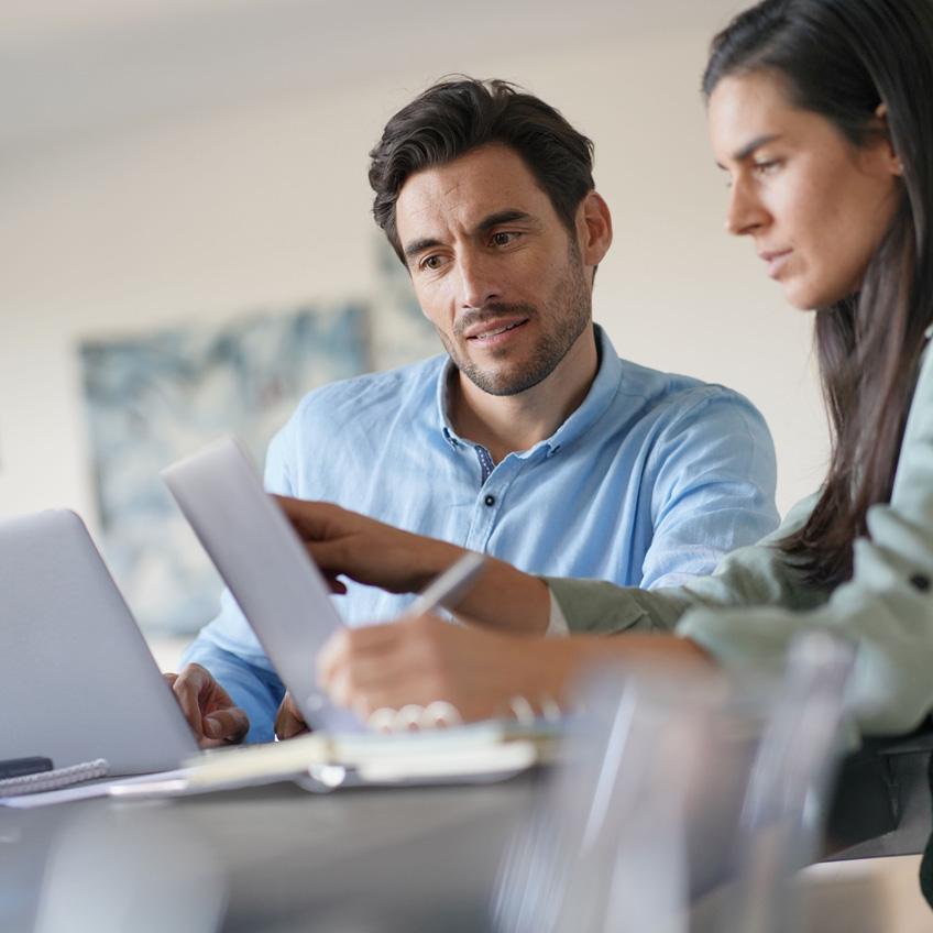 Zwei Personen an ihren jeweiligen Laptops besprechen ihre Strategien für das Datenqualitätsmanagement mit stabilen Prozessen.