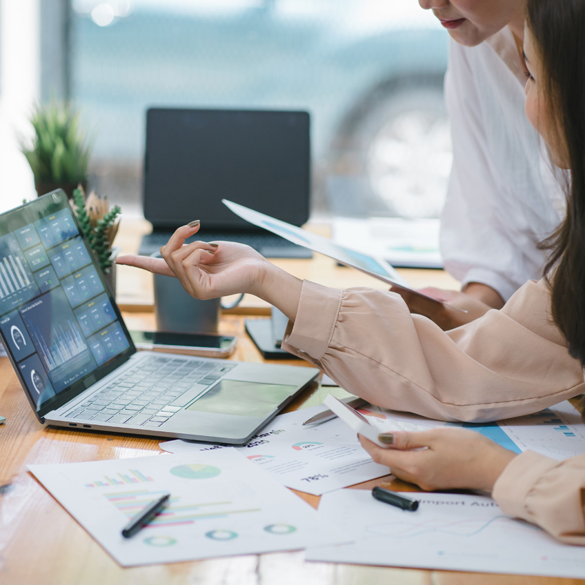 Zwei Personen besprechen ein Dokument, während eine Person auf den Laptop zeigt – Symbol für strukturiertes Datamanagement.